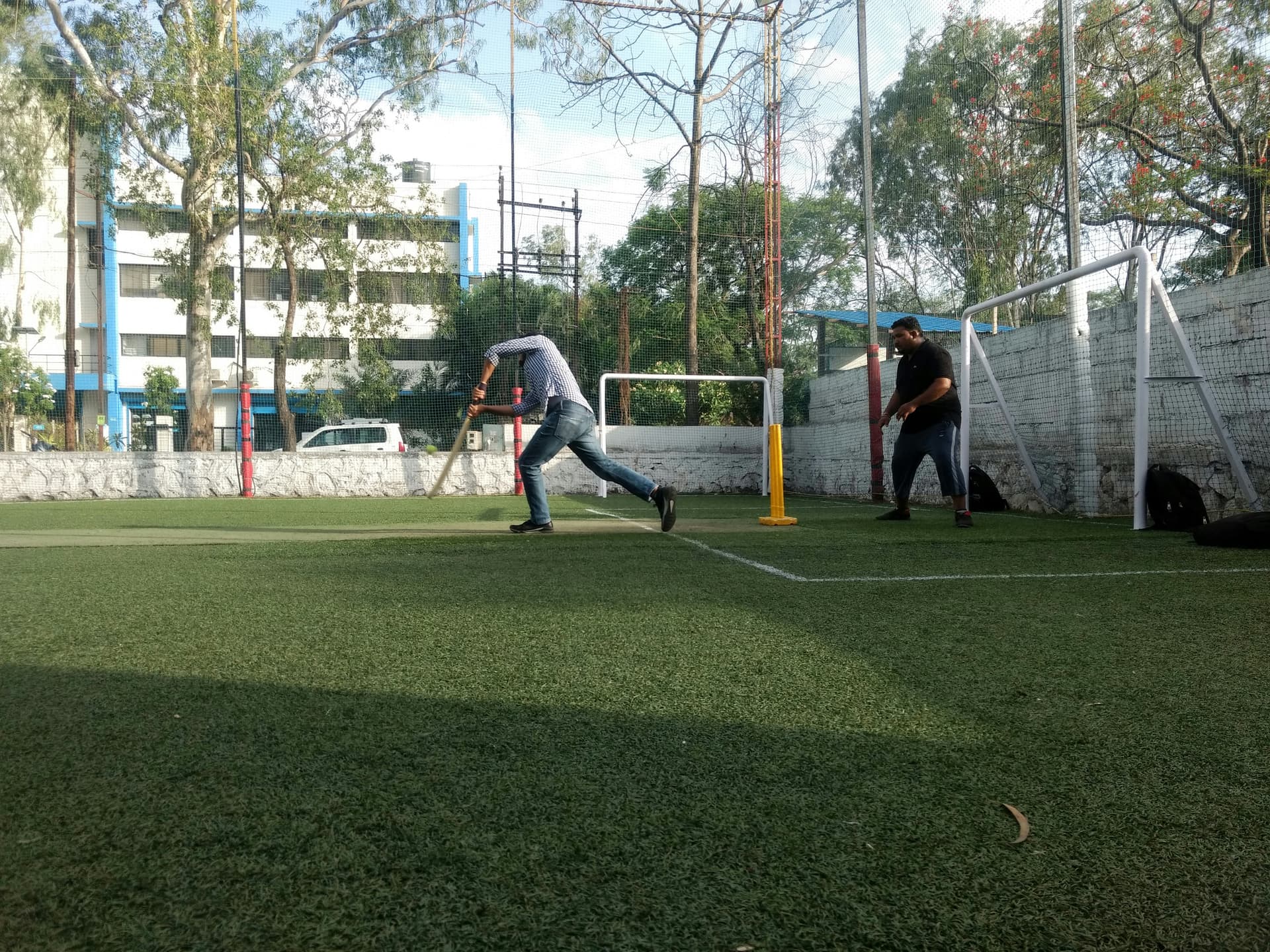 A batter drives on a larger artificial-turf cricket ground