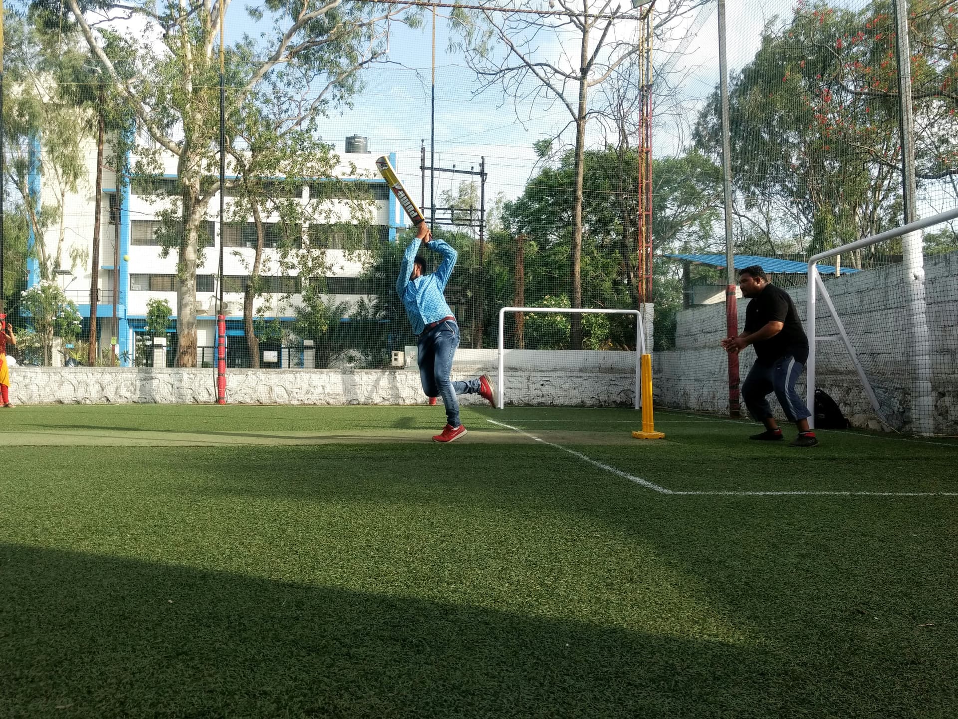 A batter lofts the ball on an enclosed artificial-turf box-cricket court
