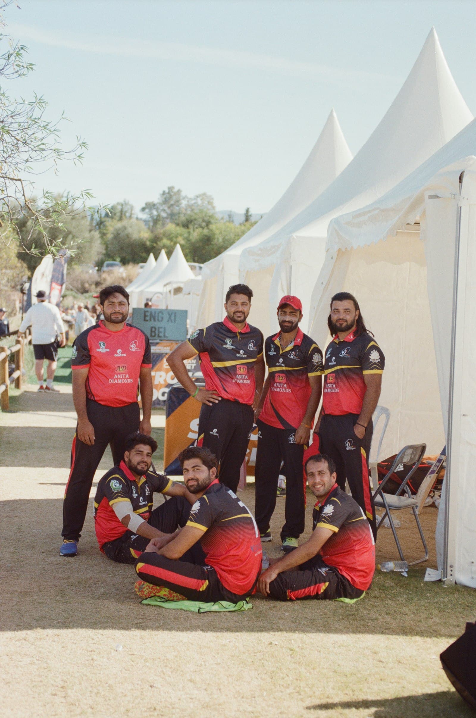A cricket team in matching red kit posing together, some standing and some crouched