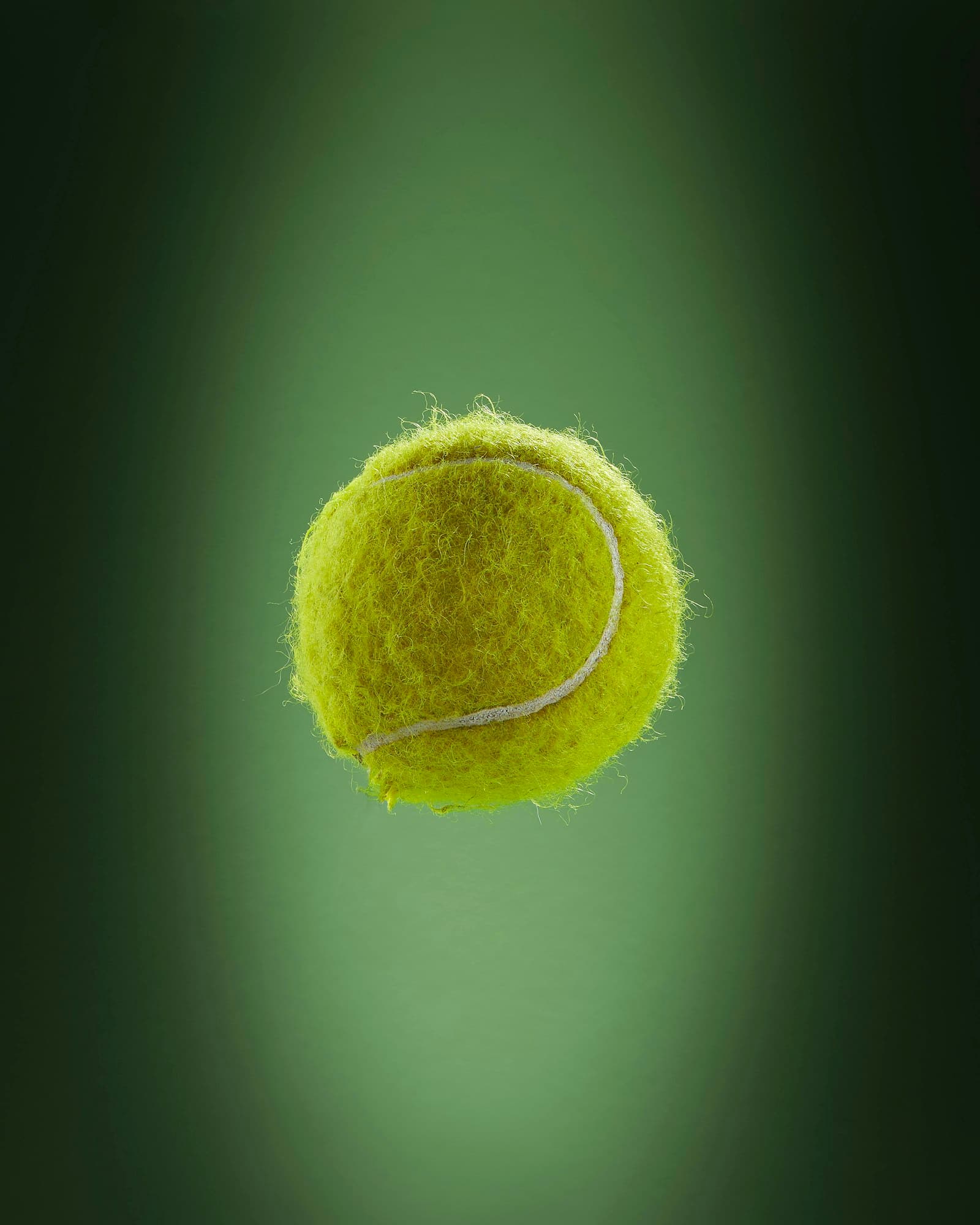 A tennis ball frozen in mid-air against a dark green background