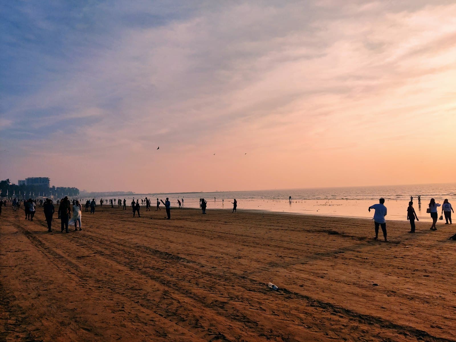 People scattered across a wide beach at dusk, drifting towards a game