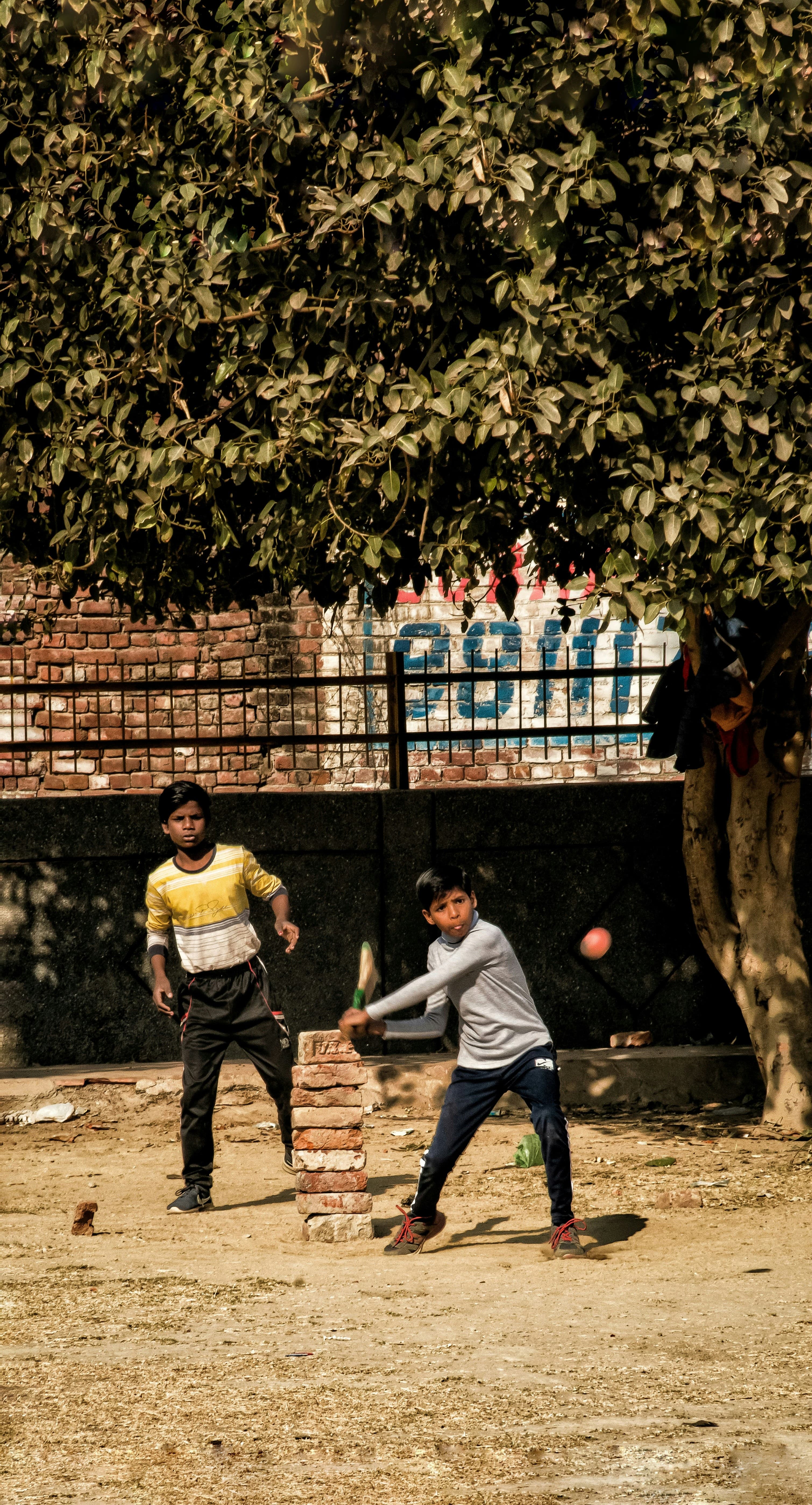 Two boys playing gully cricket with a stack of bricks for stumps