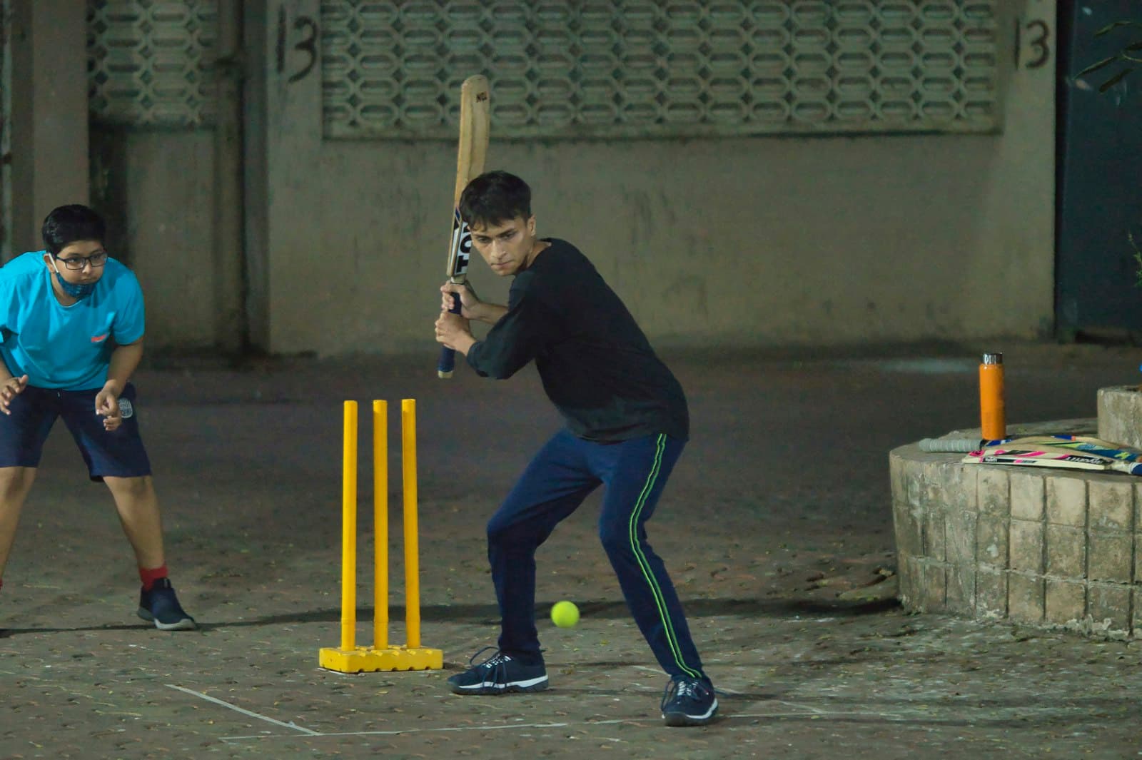 A batter and a wicket-keeper at yellow plastic stumps in a covered parking lot