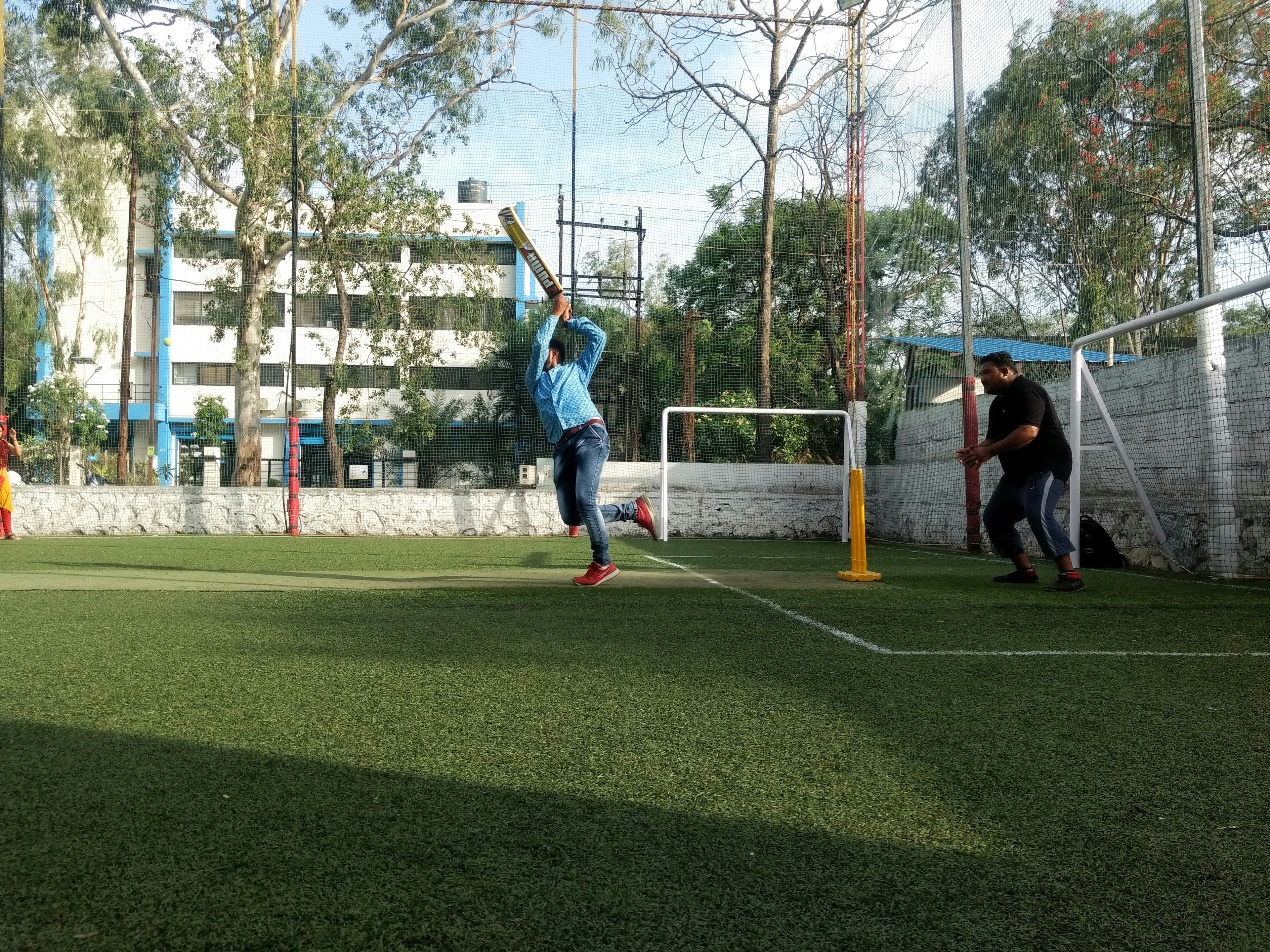 A batter lofts the ball over the bowler during a turf cricket match