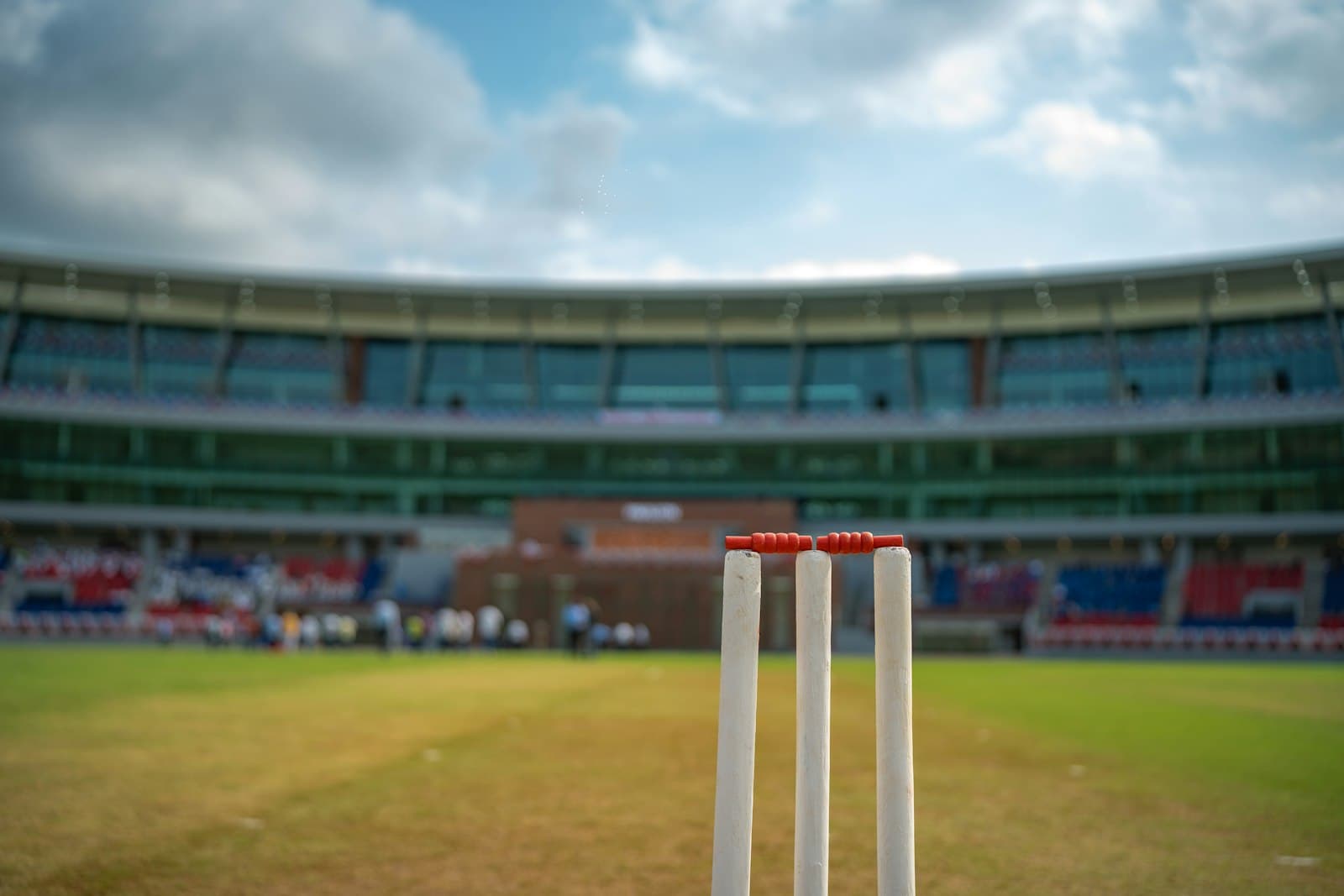 A set of cricket stumps standing alone on a pitch in front of an empty stadium