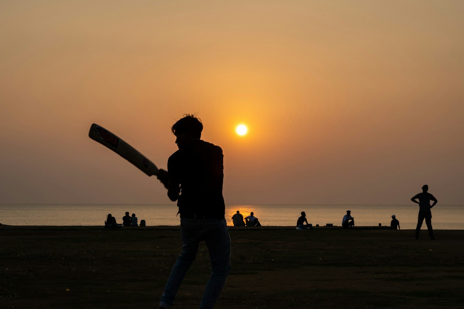 A lone batter silhouetted at sunset by the sea, bat raised