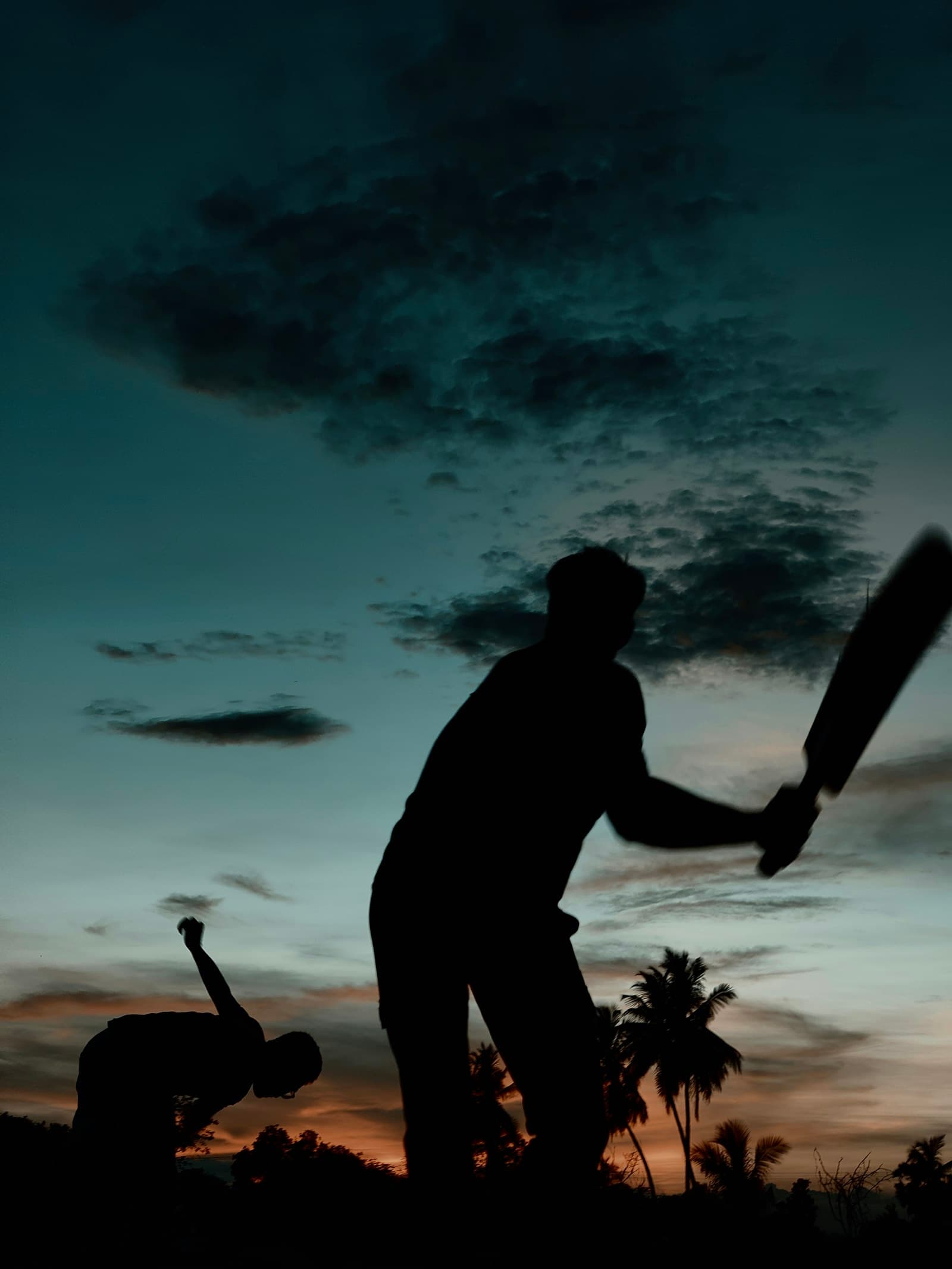 A batter and keeper silhouetted against a darkening evening sky