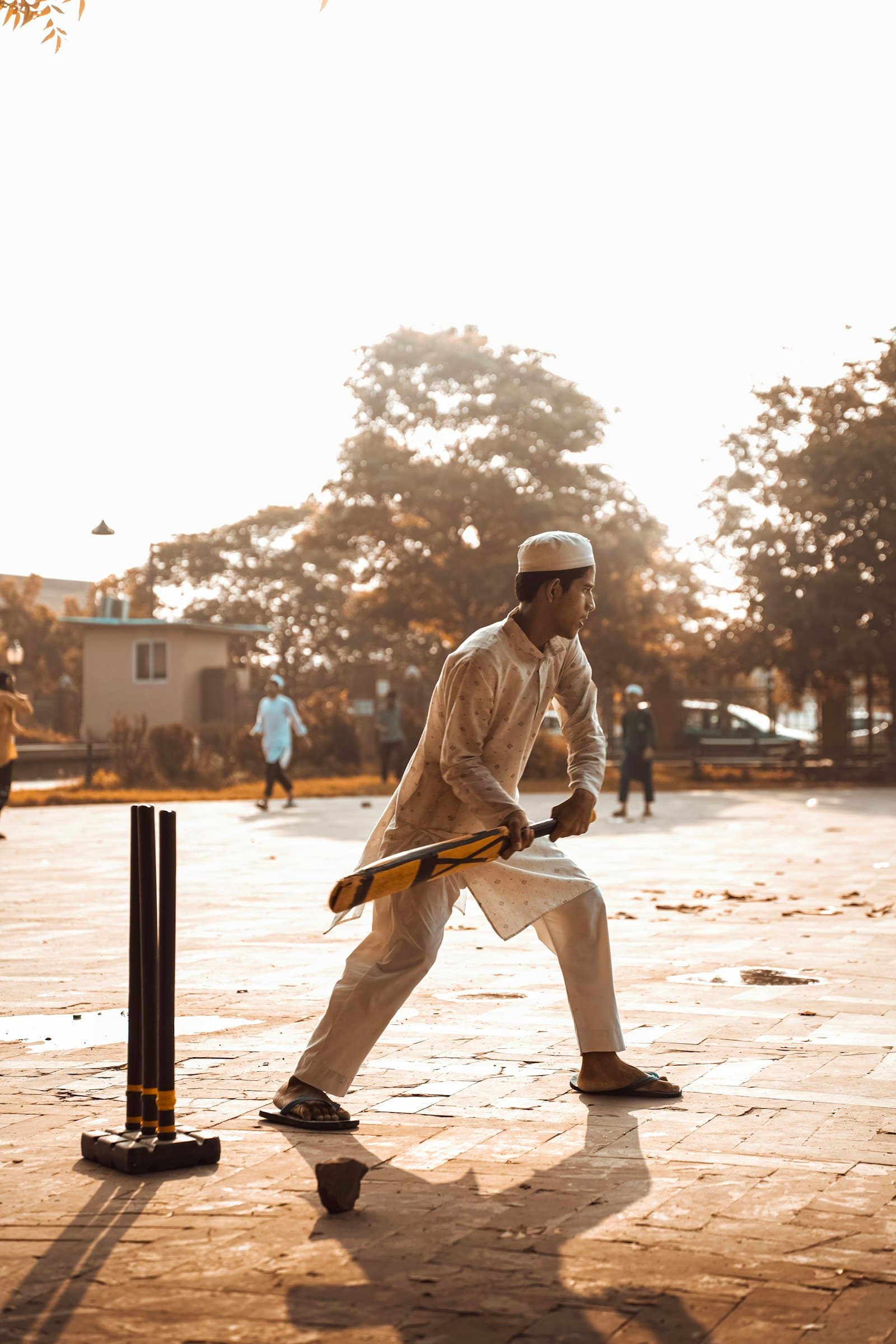 A batter alone at the crease on a dusty ground, stumps behind him in golden light