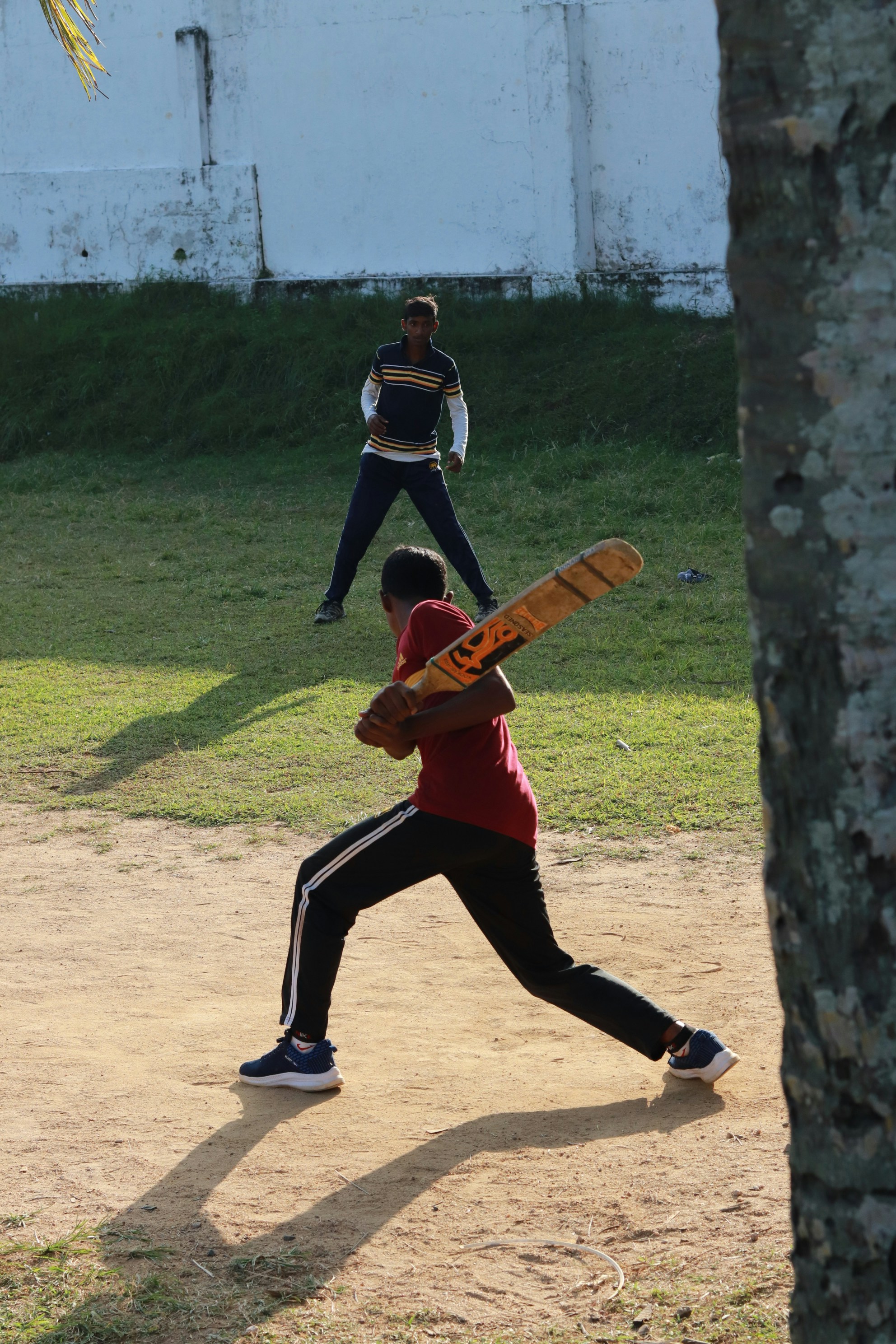 A young batter takes guard during a gully cricket match by a boundary wall