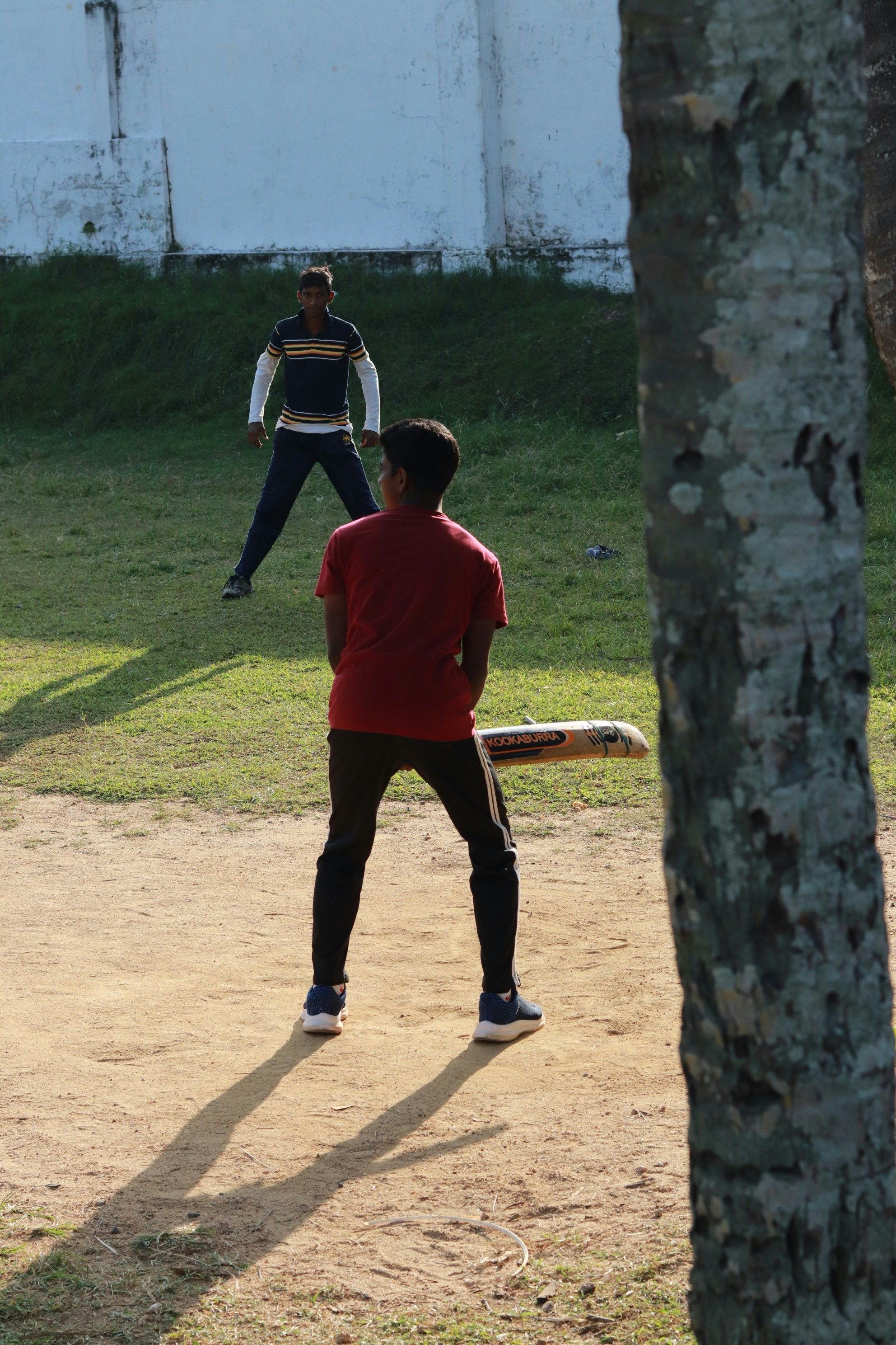 Bowler's-eye view of a batter waiting on a dusty gully cricket pitch