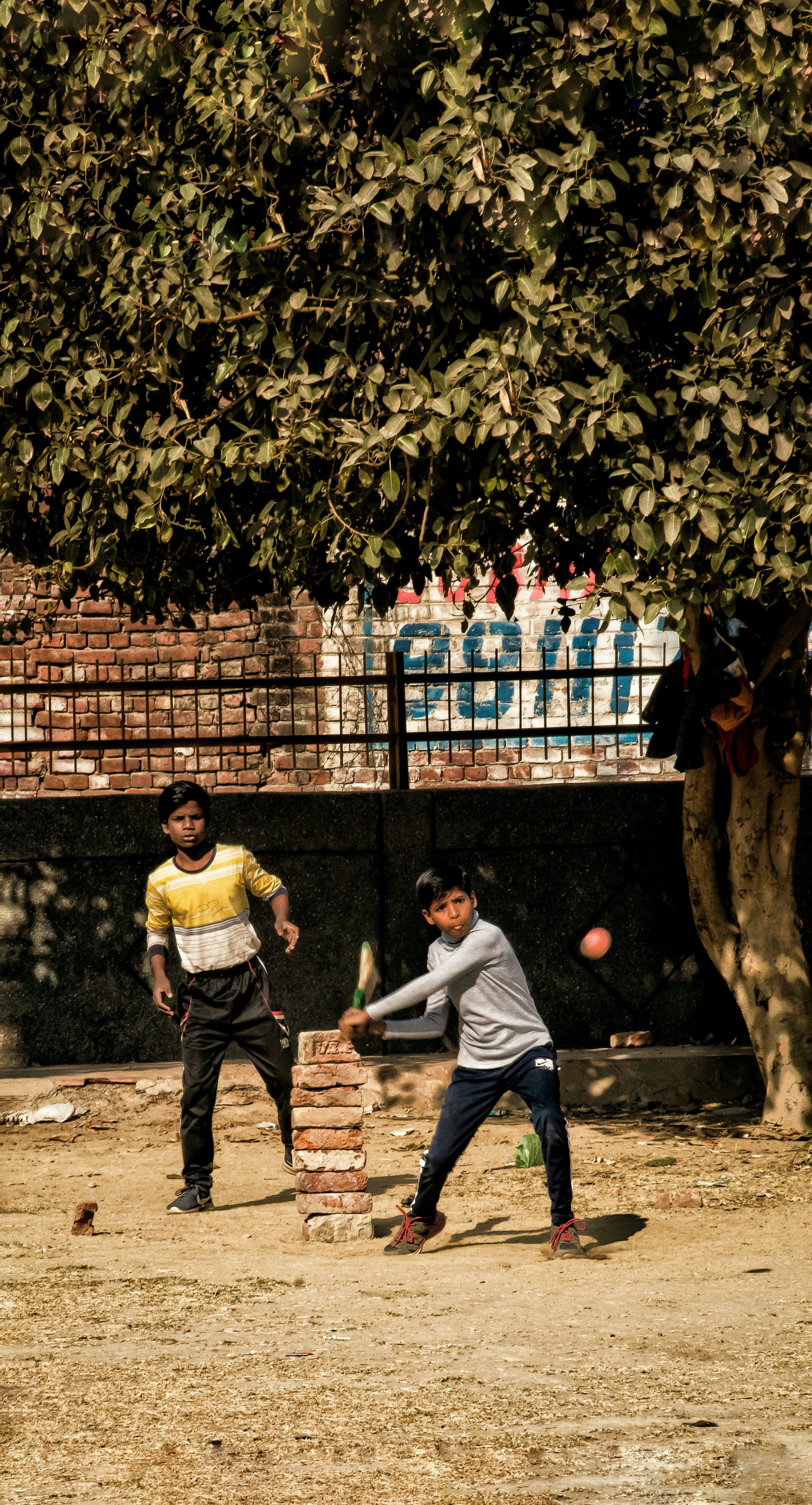 Two boys playing gully cricket with a stack of bricks for stumps